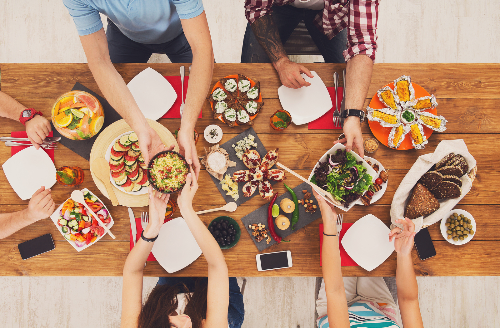 People eat healthy meals at festive table served for party. Friends celebrate with organic food on wooden table top view. Woman pass dish plate to man